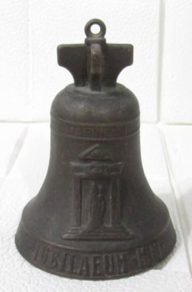 BRONZE - Uma (1) sineta em bronze decorada com santo e brasão em alto relevo, inscrições "MARINELLI JUBILAEUM M. M." e "AGNONE TOTUS TUUS", topo em formato de cruz. Altura 9,5 cm. — BRONZE