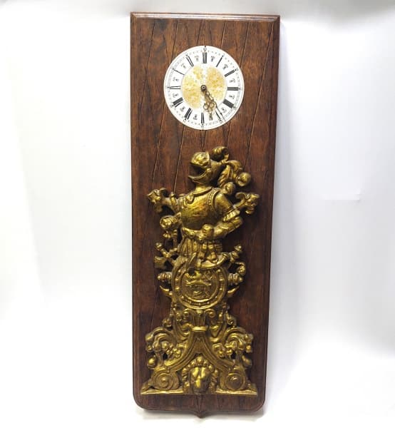 COLECIONISMO--DECORATIVO, PESADO E COMPRIDO RELÓGIO À QUARTZ DE PAREDE, EM GROSSA PLACA DE MADEIRA, NO TOM CASTOR. PARTE CENTRAL COM INTERESSANTE APLIQUE EM BRONZE DOURADO MACIÇO, RICAMENTE CINZELADO COM FIGURAS DE "ARMADURA, LEÕES E ARABESCOS". --- Med:90cm comp x 30cm larg. ---- FUNCIONAMENTO DO RELOGIO NÃO TESTADO(Sem pilhas)) — COLECIONISMO