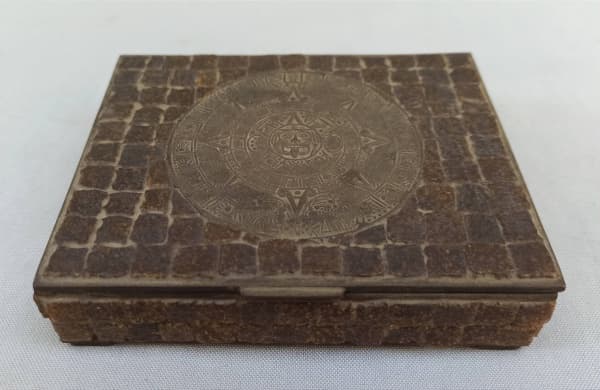 DIVERSOS, uma (1) cigarreira, confeccionada em bronze, ornamentação relevada com motivos da Antiga Civilização Asteca, arremates com apliques em pastilhas de pedra ou imitação, medindo 12,5 x 10 x 3 cm, interior com cigarros franceses da marca GITANES, não sei se estão na validade e apropriados para o consumo, somente para coleção. — DIVERSOS