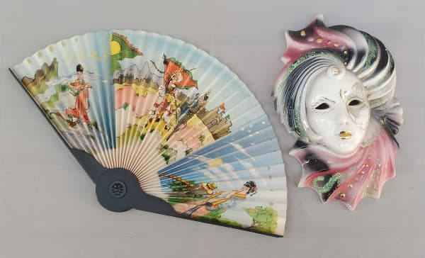 DIVERSOS, lote com dois (02) itens: 1 máscara de cerâmica branca decorada em tons de rosa, dourado e verde, padrão veneziano, para pendurar em parede, medindo 21cm de altura; 1 leque com estrutura de polímero na tonalidade preta e papel pregueado com desenho oriental, medindo fechado 20cm de altura; usados. — DIVERSOS