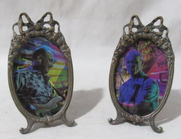 BRONZE - Par de porta-retratos ovalados em bronze e tampo de vidro, pés ondulados, decoração com frisos finalizada em flores e laço. Apresentam sinais de oxidação. Medidas 13 x 7 cm. — BRONZE