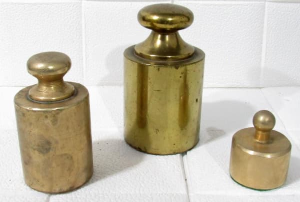 COLECIONISMO - Lote com três pesos de balança em bronze, sendo a) Um de 2kg b) Um de 1kg c) Um menor sem marcação. Medidas maior10cm, menor 5cm — COLECIONISMO