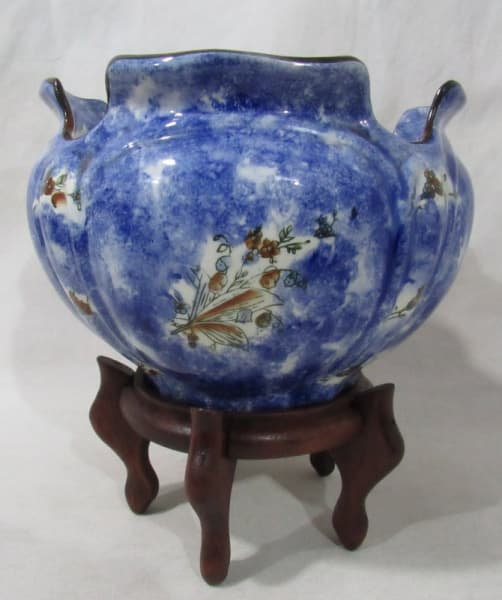 DIVERSOS - Um cachepot em porcelana MAUÁ vitrificada branca com esmaltagem azul e desenhos de flores e folhas, bordas recortadas, sobre peanha de madeira com quatro pés curvos. Medidas: 24x17cm e 11x21cm. — DIVERSOS