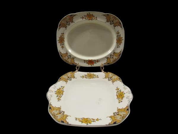 WOOD'S IVORY WARE, Inglaterra, Duas travessas ovais confeccionadas em faiança vitrificada na tonalidade creme com pintura de florões, arabescos, flores e folhagens em policromia e borda filetada na cor preta, apresentando sinais de craquele, medindo 27x21,5cm e 25,5x22cm, apresentando pequenas marcas do tempo. — WOOD'S IVORY WARE