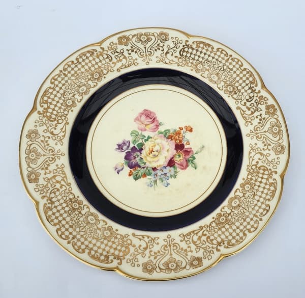 WOODS IVORY WARE, Inglaterra, Prato decorativo confeccionado em faiança vitrificada na tonalidade creme, com pintura de flores e folhagens em policromia, motivos florais com faixa na cor azul e bordas filetadas a ouro. Medindo 27,5cm — WOODS IVORY WARE